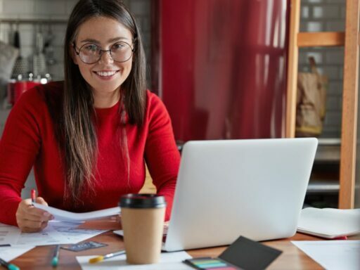 Joven mujer sonriente vestida de rojo con lentes y una computadora