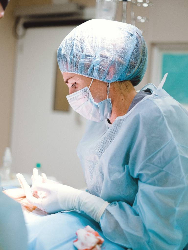 Joven médico mujer con cubre boca y bata azul en un quirófano operando